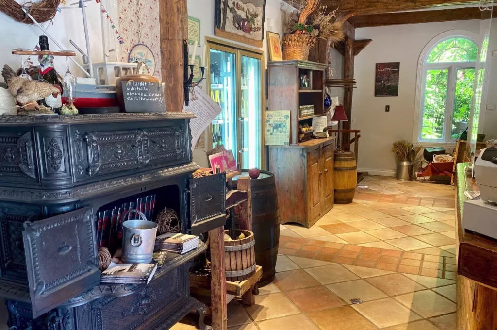 Intérieur rustique d'une boutique ou d'un musée avec un poêle à bois noir décoré, des tonneaux en bois, des meubles anciens et une grande fenêtre avec vue sur un jardin vert