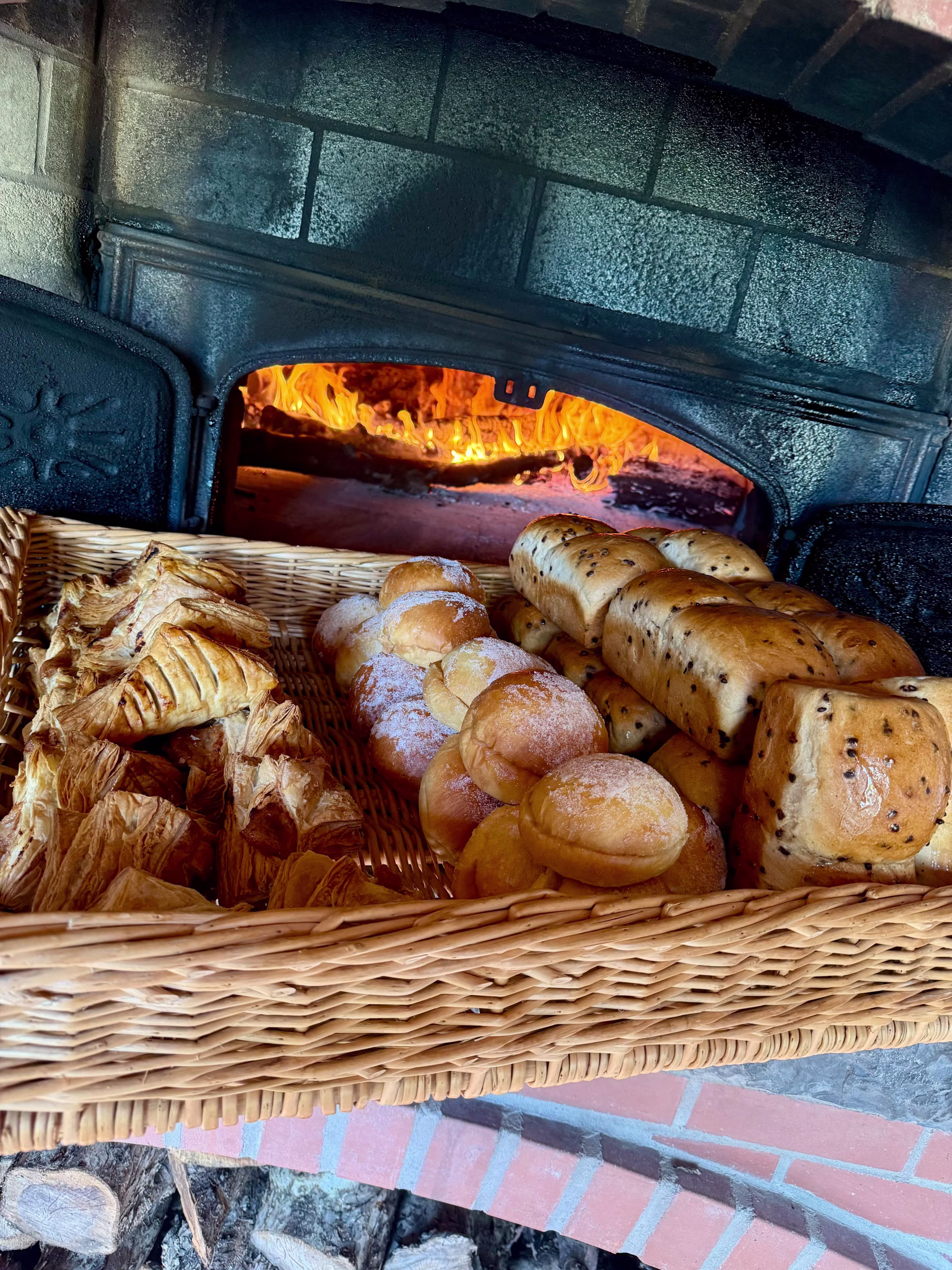 Paniers de pâtisseries et pains frais devant un four à bois en feu